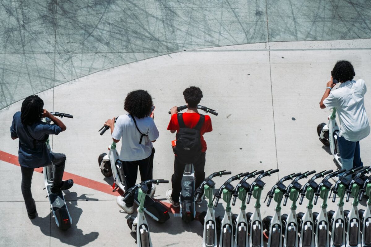 Group of young adults using electric scooters on a sunlit urban pavement.