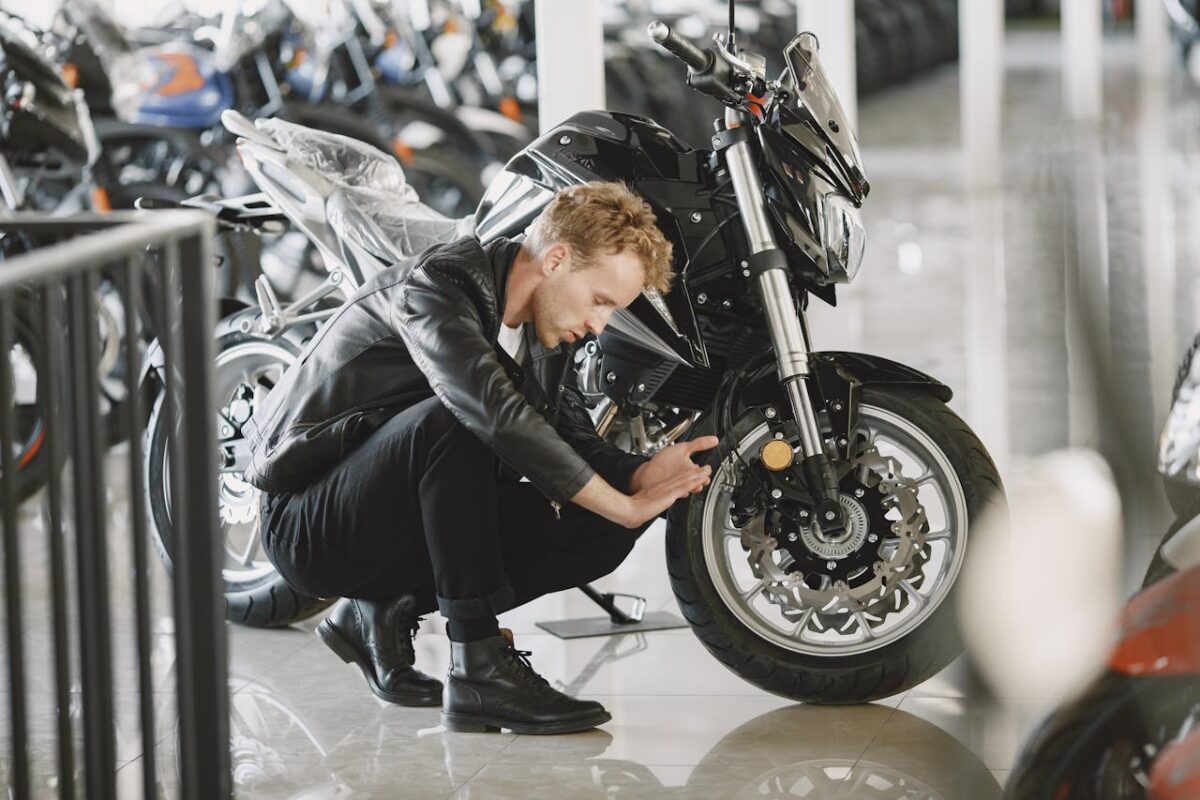 Stylish man inspecting motorcycle tire in a showroom wearing a black leather jacket.
